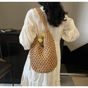 Detail view of a brown hollow-out woven straw shoulder bag worn with a white dress