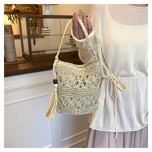 Detail of hand-woven straw bucket bag with large decorative tassels and wooden beads