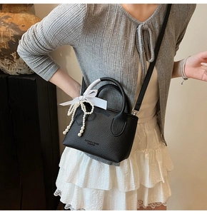 Detail of black pebbled leather bucket bag with pearl bow charm and hand strap