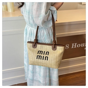 Detailed shot of beige straw tote bag featuring black embroidered letters and knotted leather straps
