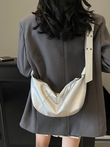 Silver metallic crescent crossbody bag with grommet wide strap worn by a model