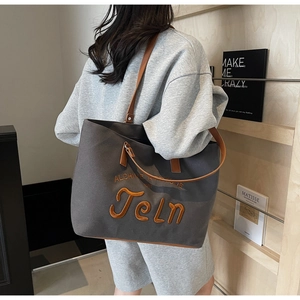 Detail of grey canvas tote bag with orange 3D embroidery and brown leather dual straps