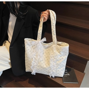 Détail du sac fourre-tout à pois blanc crème avec nœud en dentelle sur fond de bois