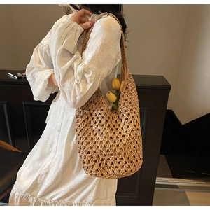 Detail of hollow woven straw bag with wide shoulder strap carried on white dress