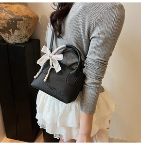 Detail of black lychee leather bucket bag with silk bow and pearl chain decoration