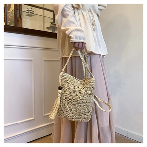 Detail of hand-woven beige bucket bag with hollow floral patterns and long fringe tassel