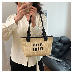 Detail of woven straw tote bag with black leather trim and knotted handle design