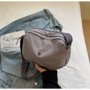 Détail du sac bandoulière en nylon mauve avec logo métallique rond et large sangle