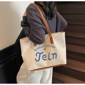 Detail of canvas tote bag with brown leather handles and blue embroidered lettering