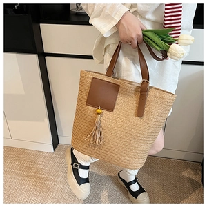 Detail of hand-woven straw tote bag with brown leather handles and a long tassel charm