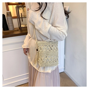 Detail of hand-woven beige bucket bag featuring hollow floral patterns and long tassels