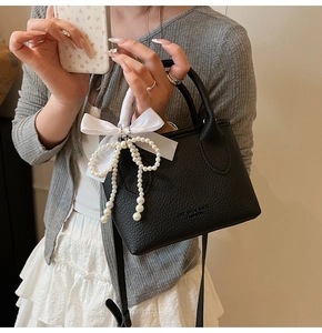 Detailed view of black pebbled leather bucket bag with pearl bow and ribbon charm
