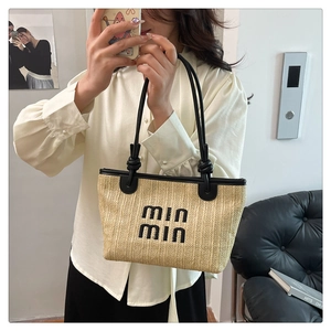 Detail of hand-woven straw tote with black logo embroidery and knotted leather handles