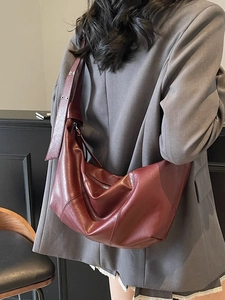 Deep red crescent shoulder bag in glossy leather worn by a model in a grey suit