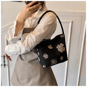 Detail of black bucket bag with white floral embroidery and thin shoulder strap