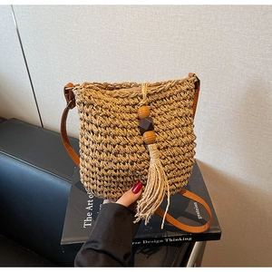 Dettaglio della borsa a secchiello in paglia intrecciata con perline e nappa boho