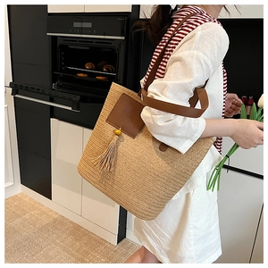 Detail of woven straw tote bag featuring leather trim, tassel pendant and brown strap