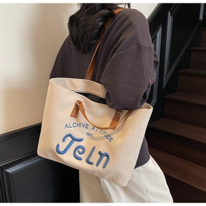 Detail shot of beige canvas tote bag featuring blue embroidery and brown leather straps
