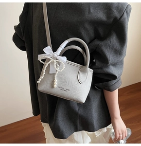Detailed side view of a grey bucket bag with a white silk bow and pearl tassel pendant