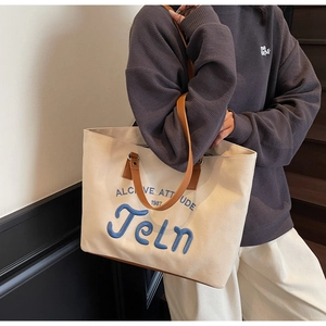 Close-up of canvas tote bag featuring blue letter embroidery and brown leather trim
