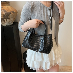 Détail d'un sac seau en cuir tressé noir avec poignées supérieures et bandoulière fine