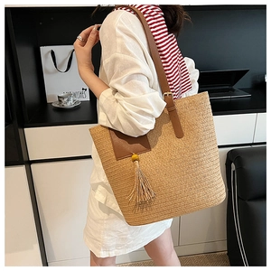 Detail of straw tote bag with brown leather straps and woven tassel in modern setting