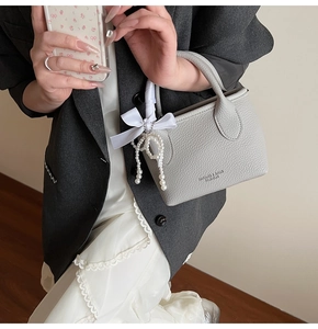 Close-up of grey litchi texture bucket bag with white silk ribbon and pearl charm detail