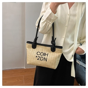 Close-up of woven straw tote bag featuring black lettering and leather knot handles