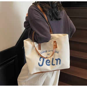 Detail of canvas tote bag showing blue 3D embroidery and leather trim stitching
