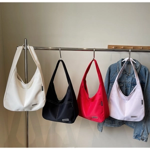 Row of minimalist hobo bags in white, black, red, and lilac hanging on a metal rack