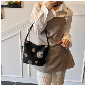 Close-up of black canvas bucket bag featuring white floral embroidery and short shoulder strap