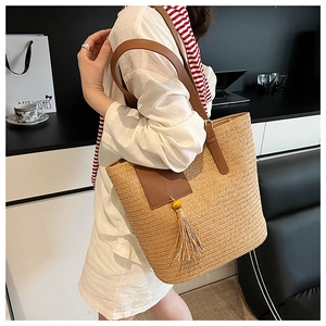 Macro detail of straw woven tote bag featuring brown leather patch and beaded tassel