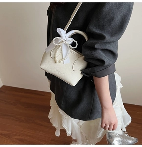 Detail of white bucket bag featuring a silk bow and pearl bead handle decoration