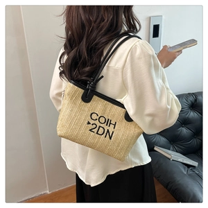 Shoulder view of a woven straw tote bag with black leather straps and text detail
