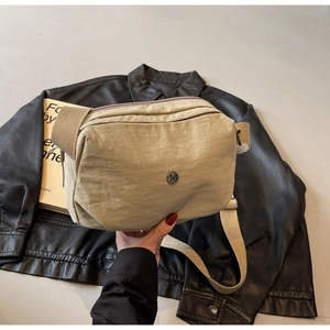Détail du sac à bandoulière beige en nylon avec logo métallique rond et sangle large