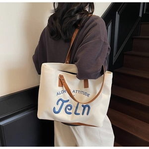 Detail of blue towel embroidered letters on cream canvas tote with brown leather strap