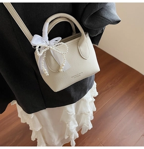 Close-up of beige lychee leather bucket bag featuring silk bow and pearl pendant details