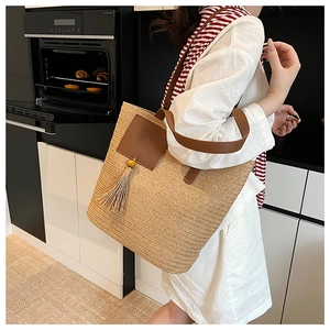Detail of summer straw woven tote bag featuring brown leather patch and beaded tassel