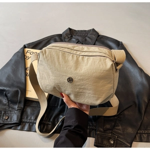 Détail du sac bandoulière en nylon beige avec tissu imperméable et logo métallique
