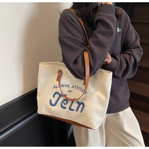 Detail view of canvas tote bag with letter embroidery and contrast brown leather straps