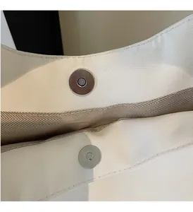 Close-up of silver magnetic clasp on white canvas tote bag with herringbone lining