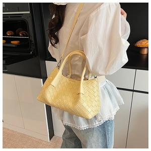 Gros plan d'un sac à main en cuir tressé jaune pâle porté par un mannequin en cuisine