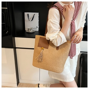 Detail of summer straw tote bag with brown leather straps and yellow tassel accessory