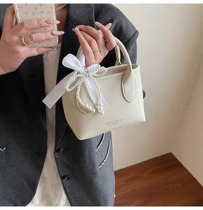 Close-up of cream lychee leather bucket bag with silk bow and pearl chain handle details