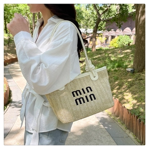 Detail of straw woven tote bag featuring white leather straps and black embroidered text