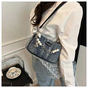 Détail du sac bandoulière en denim avec chaîne perlée, nœud argenté et logo mode