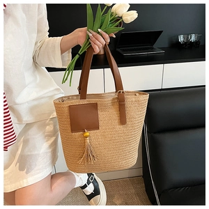 Detail of woven straw tote bag featuring brown leather trim and long tassel accents