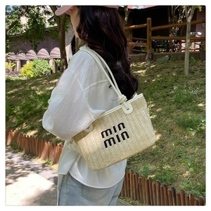 Detail of woven straw tote bag with black lettering and knotted white leather handle