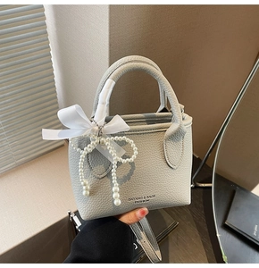 Detail of light gray lychee grain leather bucket bag with bow and pearl tassel