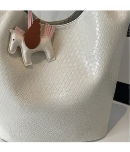 Close-up of white woven leather bucket bag featuring a Pegasus charm accessory